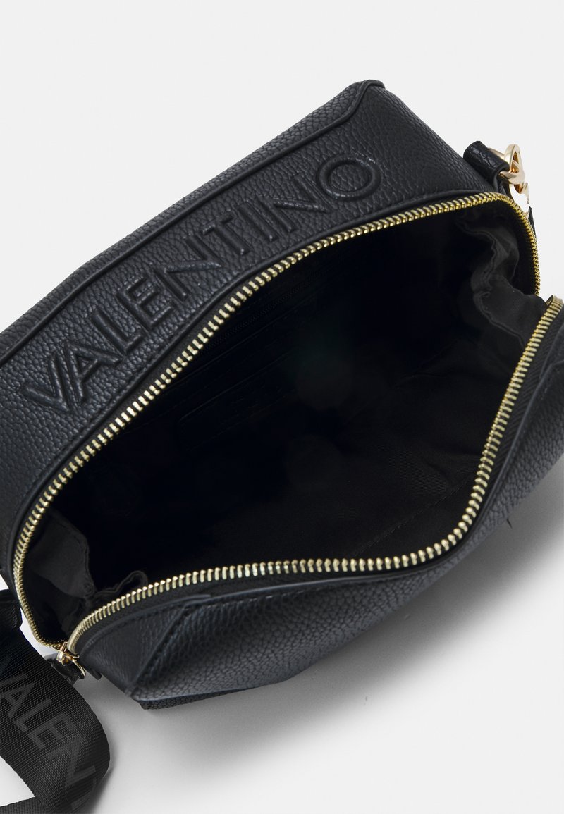 Bolso de cuero negro con exterior texturizado, cierre de cremallera dorada y interior forrado de tela. Presenta un logo en relieve en la parte superior.