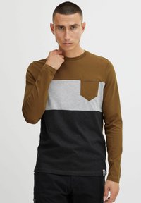 Dugi rukav T-shirt izrađen od pamuka, s smešnim gornjim delom, sivo srednjim delom i crnim donjim delom, s džepom na grudima i teksturiranom tkaninom.