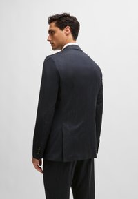 Dark grey suit jacket featuring a textured finish, dual back vents, and four-button cuffs, presented from a rear angle.