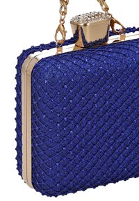 Fialové třpytivé psaníčko s tkanou texturou, zlatými kovovými prvky a drahokamovou sponou. Má řetízkové ucho pro snadné nošení.