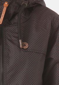 Svart tygjacka med ett fint rödprickigt mönster, utrustad med dragkedja, justerbar huva och läderdetalj på dragkedjans dragare.