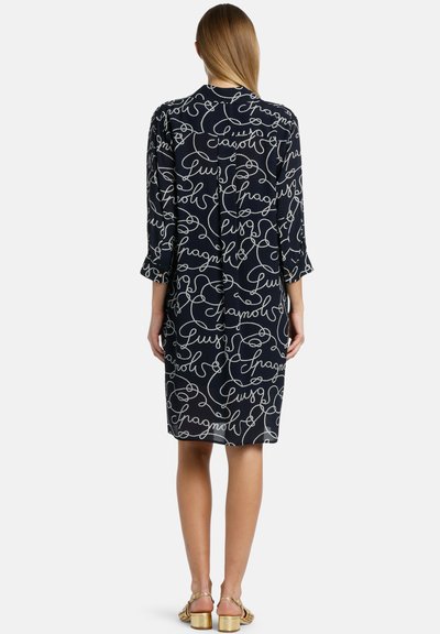 Rochie bleumarin cu model alb în scris, cu mâneci până la trei sferturi și o croială lejeră. Prezintă un decolteu rotund și se termină la jumătatea gambei.