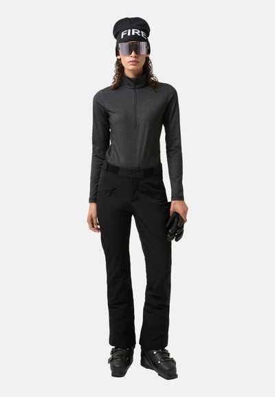 Sort zip-up langærmet trøje, sorte skibukser med detaljerede lommer, sorte handsker og skistøvler. Tilbehøret inkluderer en sort hue med "FIRE" og solbriller.