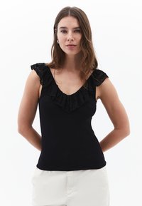 Musta hihaton toppi, jossa on röyhelöinen pitsikaulus, istuva malli ja hihaton rakenne. Sileä pinta, yhdistetty vaaleisiin alaosiin.