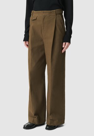 Bruine wijde broek van textuurstof, met een zijzak met een gouden knop en een hoge taille. G gedragen met een zwart top.