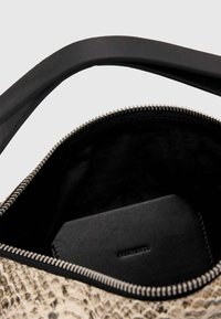 Beige laukku, jossa on käärmeennahkakuosi, musta vuori, hopea vetoketju ja musta nahkakorttikotelo sisällä. Kaareva musta kahva.