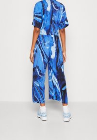 Mono de patrón azul con mangas cortas y un diseño de piernas anchas. Presenta una textura veteada con acentos en blanco y negro.