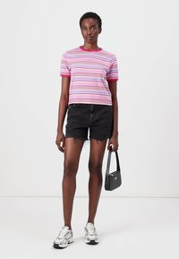 Striped short-sleeve T-shirt in pink, purple, and white, paired with black denim shorts. Model holds a small black handbag. Silver sneakers.