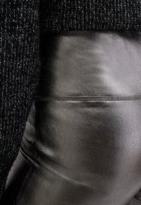 Tessuto a maglia nera sovrapposto a pelle nera liscia. Il tessuto a maglia presenta un motivo testurizzato, mentre la pelle appare lucida con un dettaglio di cucitura visibile.