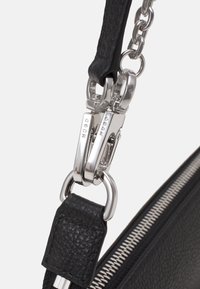 Czarna torebka z teksturowanej skóry z srebrnymi okuciami, wyposażona w masywny łańcuchowy pasek i zapięcie na zamek, z widocznym szczegółowym szyciem i akcentami.