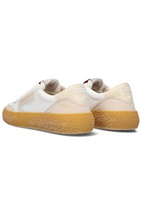 Witte en crèmekleurige sneakers met een gestructureerde bovenkant, een rubberen gumzool en een eenvoudiger design. Kenmerken zijn branding op de hiel en zijstrepen.
