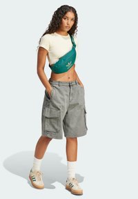 Heled hallid korvpallilühikesed püksid, koos kreemja sobiva T-särgiga ja rohelise õlalhinnaga kotiga, millel on Adidas logo. Roheline aktsentidega tossud.