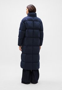 Námorná pufrová bunda s vysokým golierom, prequiltným dizajnom a dlhým strihom. Vyrobená z jemného, textúrovaného materiálu. Vhodná na chladné počasie.