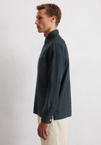Chemise à manches longues vert foncé avec col, poche poitrine unique et poignets à boutons. Fabriquée en tissu léger avec une coupe décontractée.