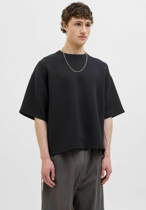 Sort oversized sweatshirt med korte ærmer, lavet af blød kvalitet. Har en rund hals og en diskret kant. Sammen med grå bukser.