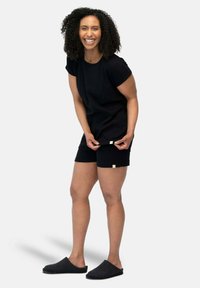 Top corto nero a maniche corte e pantaloni corti realizzati in tessuto morbido, con una vestibilità rilassata. Dettagli notevoli includono piccoli loghi sui pantaloni corti.