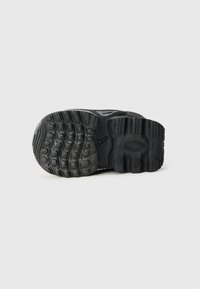 Semelle de chaussure en caoutchouc noir avec motifs de grip texturés, bout rond, design de sculpture proéminent et un accent de logo sur le côté.