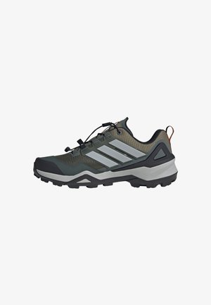 Scarpa da hiking da esterno in verde e nero con suola grigia, tre strisce riflettenti e un sistema di lacci rapidi sulla parte superiore.