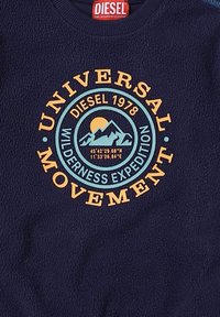 Felpa in pile navy con una grafica circolare che presenta montagne, un sole e la scritta: "Universal Movement Diesel 1978 Wilderness Expedition."
