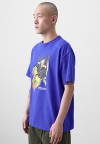 T-shirt en coton violet avec un graphique coloré d'un toucan sur le devant, à manches courtes et à la coupe décontractée.