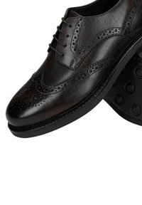 Zwarte leren veterschoen met broguedetails, een afgeronde neus, vijf veterogen en een rubberen buitenzool met ronde gripjes.