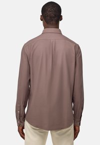 Camicia a maniche lunghe in tessuto mauve tenue, con polsini abbottonati, un yoke posteriore e un orlo dritto. Texture liscia e design semplice.