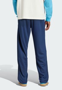 Blue athletic pants in a soft, textured material with a loose fit. Features zippered sides and a minimalistic design.