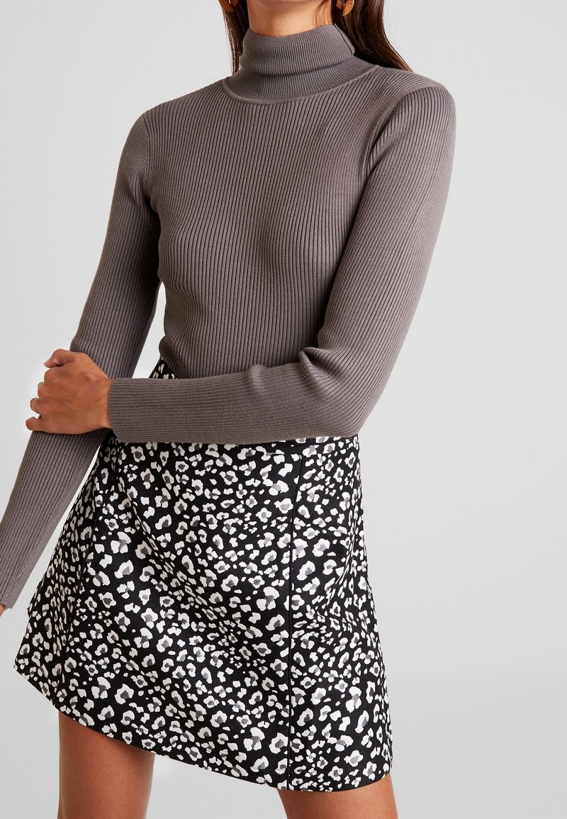 Grå randig polotröja i kombination med en svart kjol som har ett vitt leopardmönster, vilket framhäver textur och kontrasterande mönster.