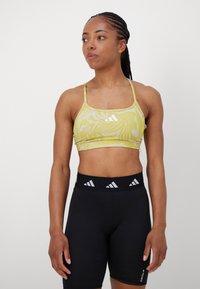 Sostén deportivo amarillo con un patrón en espiral, con tirantes finos y escote en forma de barco. Combinado con pantalones cortos negros de talle alto con acentos de logo.