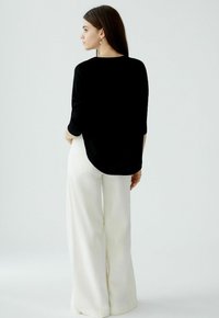 Schwarzes Oberteil mit drei Viertelärmeln und abgerundetem Saum, kombiniert mit weißen weit geschnittenen Hosen, was eine kontrastreiche Farbpalette schafft.