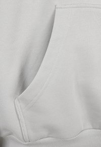 Närbild av en grå tyg hoodie-ficka med synliga stygn och ribbad midja i botten.