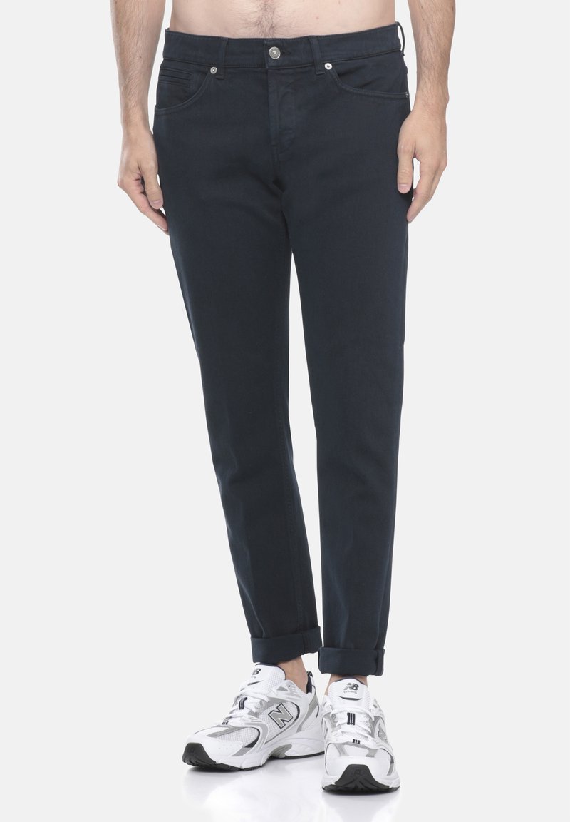 Pantaloni blu navy realizzati in tessuto di cotone, con una vestibilità slim, orli risvoltati e tasche sottili; abbinati a scarpe da ginnastica bianche.