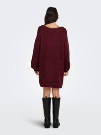 Suéter de punto oversize burdeos con un escote amplio y mangas largas, combinado con botas negras hasta la rodilla, que exhibe una tela texturizada.