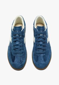 Sneaker in suede blu con accenti bianchi, punta tonda, lacci texture e suola in gomma. Il design presenta una finitura liscia e morbida.