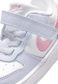 Hvit og rosa Nike barne-sneaker med borrelås, lisser og rosa Nike-swoosh på siden.