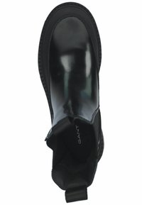 Botte de cheville noire avec une finition brillante, bout rond, panneaux latéraux extensibles et semelle en caoutchouc texturée avec une languette. Logo de la marque visible à l'intérieur.