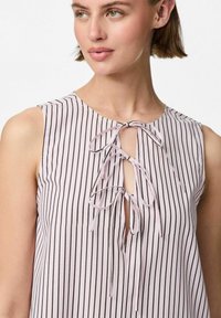 Top sin mangas rosa claro con rayas negras verticales, que presenta un escote en forma de llave con lazos de cinta. Tejido suave con una textura lisa.
