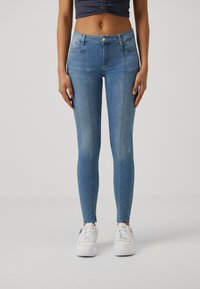 Jeans ajustados de mezclilla azul desgastada con cintura alta, que cuentan con bolsillos frontales, cierre de botón y un ajuste ceñido hasta el tobillo.