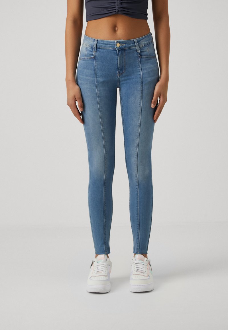 Jeans ajustados de mezclilla azul desgastada con cintura alta, que cuentan con bolsillos frontales, cierre de botón y un ajuste ceñido hasta el tobillo.