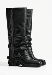 Knee-high black leather boots with a slouchy design, accented by side fringes and a strap with a buckle. Square toe and low block heel.