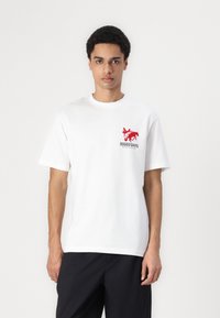 Hvid bomulds t-shirt med et rødt grafisk tryk af en hest og teksten "RODEO DAYS" på venstre bryst. Korte ærmer og rund hals.