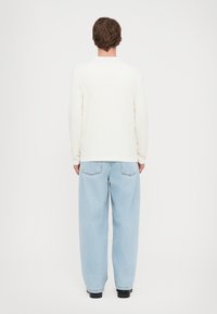 En langermet kremfarget skjorte kombinert med lyseblå baggy jeans. Skjorten har en rund hals, og jeansene har baklommer og en avslappet passform.