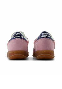 Rosa mockasnörskor med en vit och marinblå hälkappa, med en sula av gummirubber. "New Balance"-logotyp på hälen och tungan.