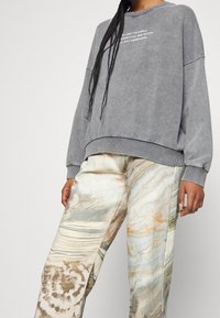 Szara bluza z okrągłym dekoltem i luźnym krojem, z białym napisem. Wzorzyste, półdopasowane spodnie w kremowych, beżowych i pomarańczowych odcieniach z falistymi wzorami.