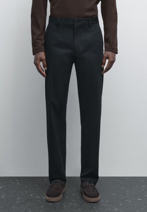 Black trousers with a straight cut, crafted from a smooth fabric, featuring a button closure and side pockets. Paired with dark brown shoes.
