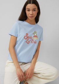 Lichtblauwe katoenen t-shirt met een "Sea La Vie" graphic in roze en groen, gecombineerd met crèmekleurige wijde broek.