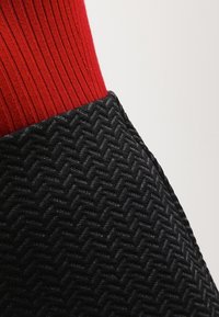 Un tissu noir texturé présente un motif en chevrons, associé à un textile rouge vibrant à côtes en haut, créant un contraste saisissant.