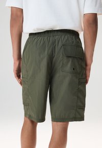 Shorts cargo in verde oliva scuro, realizzati in tessuto strutturato, con cintura elastica e tasche laterali per riporre oggetti.