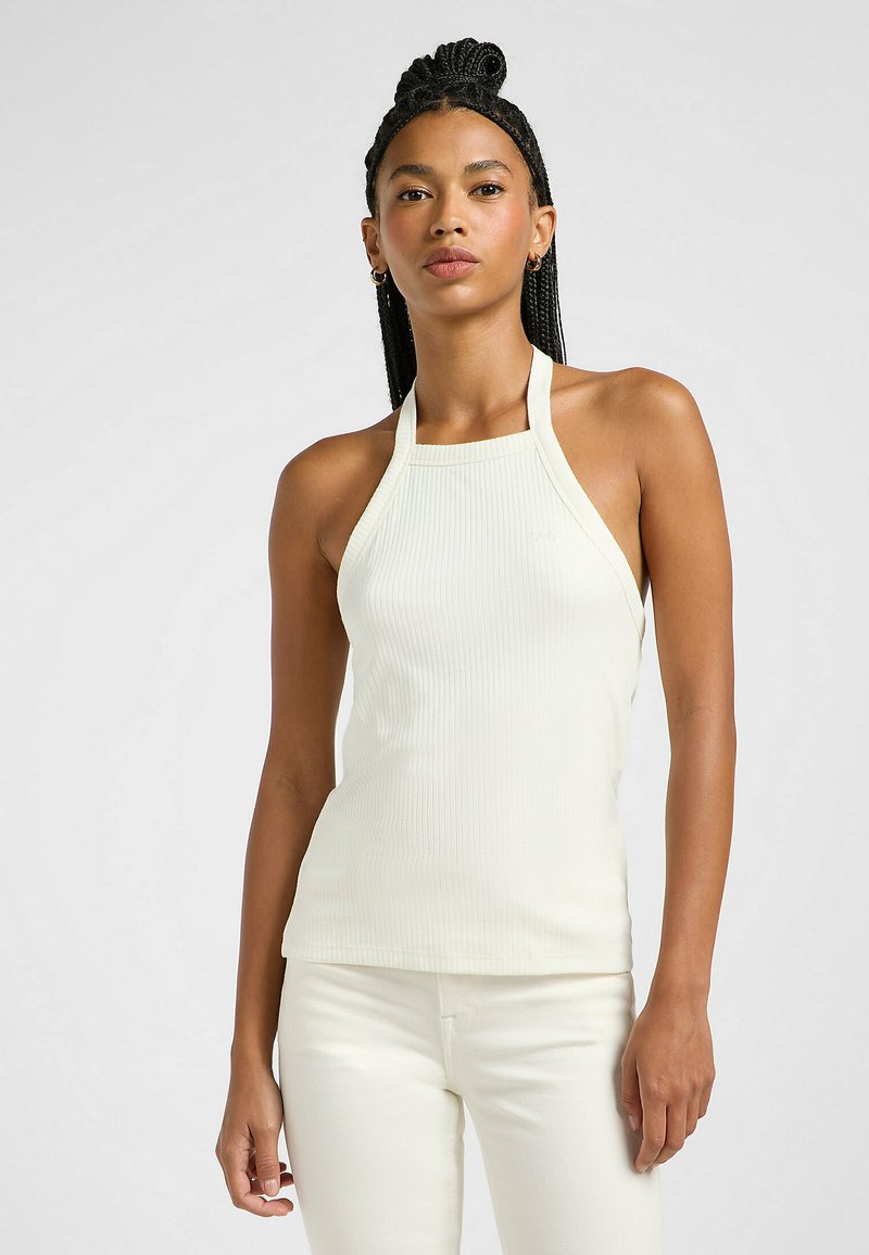 Halter neck-topp i ljus крем, ribbad textur, figurnära design. Matchar med ljus kremfärgade jeans för en sammanhängande look.