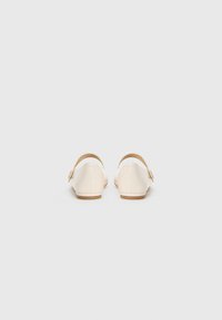 Pair of cream-colored patent leather Mary Jane flats with round buckle straps, shown from the back on a plain white background.